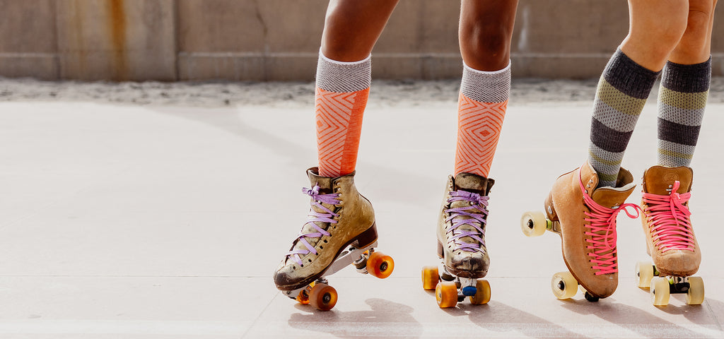 Two roller skaters wearing knee high graduated compression socks in fun and bright colors and designs.